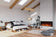 Load image into Gallery viewer, Napoleon Astound FlexMount 62-inch electric fireplace NEFL62AB recessed into a white brick feature wall in a Scandinavian-style bedroom with exposed wood ceiling beams.
