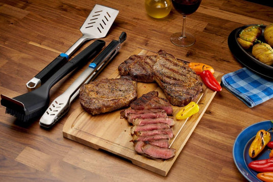 Napoleon GATL002 grilling tools displayed beside grilled steaks and vegetables on an outdoor dining table
