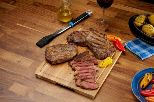 Napoleon GATL005 Silicone Basting Brush displayed beside grilled steaks, roasted peppers, and vegetables on a wooden table