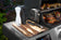 Load image into Gallery viewer, Napoleon Prestige PRO 500 side shelf with cutting board and seasonings beside food on the grill
