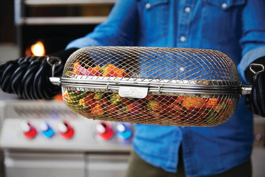 Napoleon rotisserie grill basket made of stainless steel, shown with cooked wings and vegetables on a barbecue grill