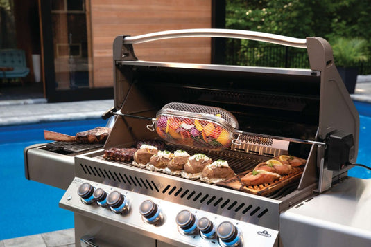 Napoleon rotisserie grill basket made of stainless steel, shown with cooked wings and vegetables on a barbecue grill