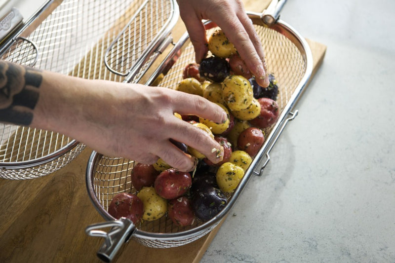 Load image into Gallery viewer, Napoleon rotisserie grill basket made of stainless steel, shown with cooked wings and vegetables on a barbecue grill
