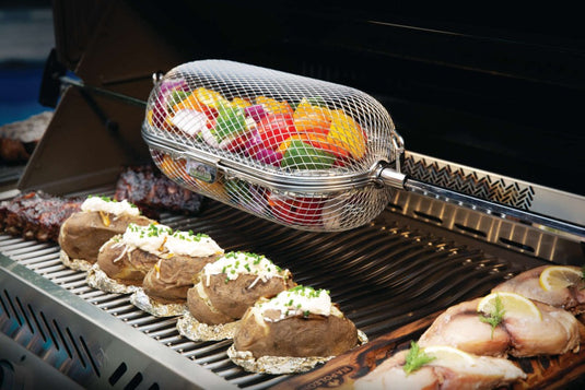 Napoleon rotisserie grill basket made of stainless steel, shown with cooked wings and vegetables on a barbecue grill
