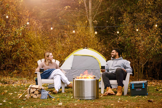 Napoleon Timberwolf stainless steel smokeless fire pit burning outdoors beside a tent and two campers
