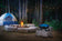Load image into Gallery viewer, Napoleon TravelQ 285 blue portable propane gas grill at a forest campsite beside a tent and campfire
