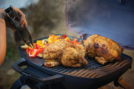 Two chickens being grilled on Napoleon TravelQ 285 Red Portable Gas Grill with vegetables.